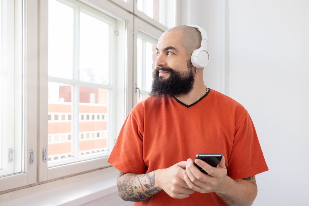 A person is looking out the window, listening to an Accessibility Library Celia audiobook on a mobile phone using the Pratsam Reader application.