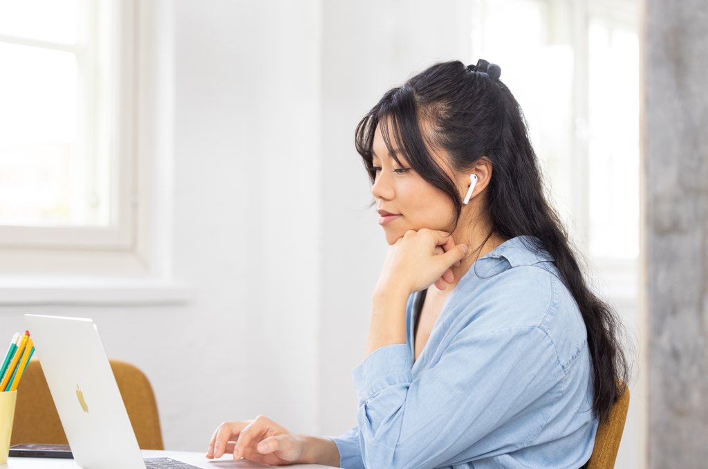 A person is sitting at a table with headphones on with a computer in front of them. Photo Accessibility Library Celia.